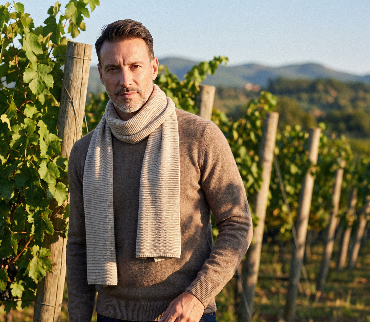 Uomo con sciarpa e maglione in cashmere tra i filari