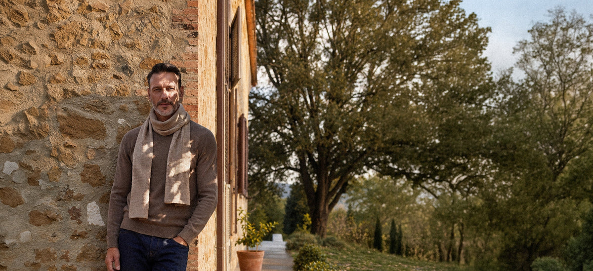 Uomo con maglione e sciarpa in cashmere davanti a un casale
